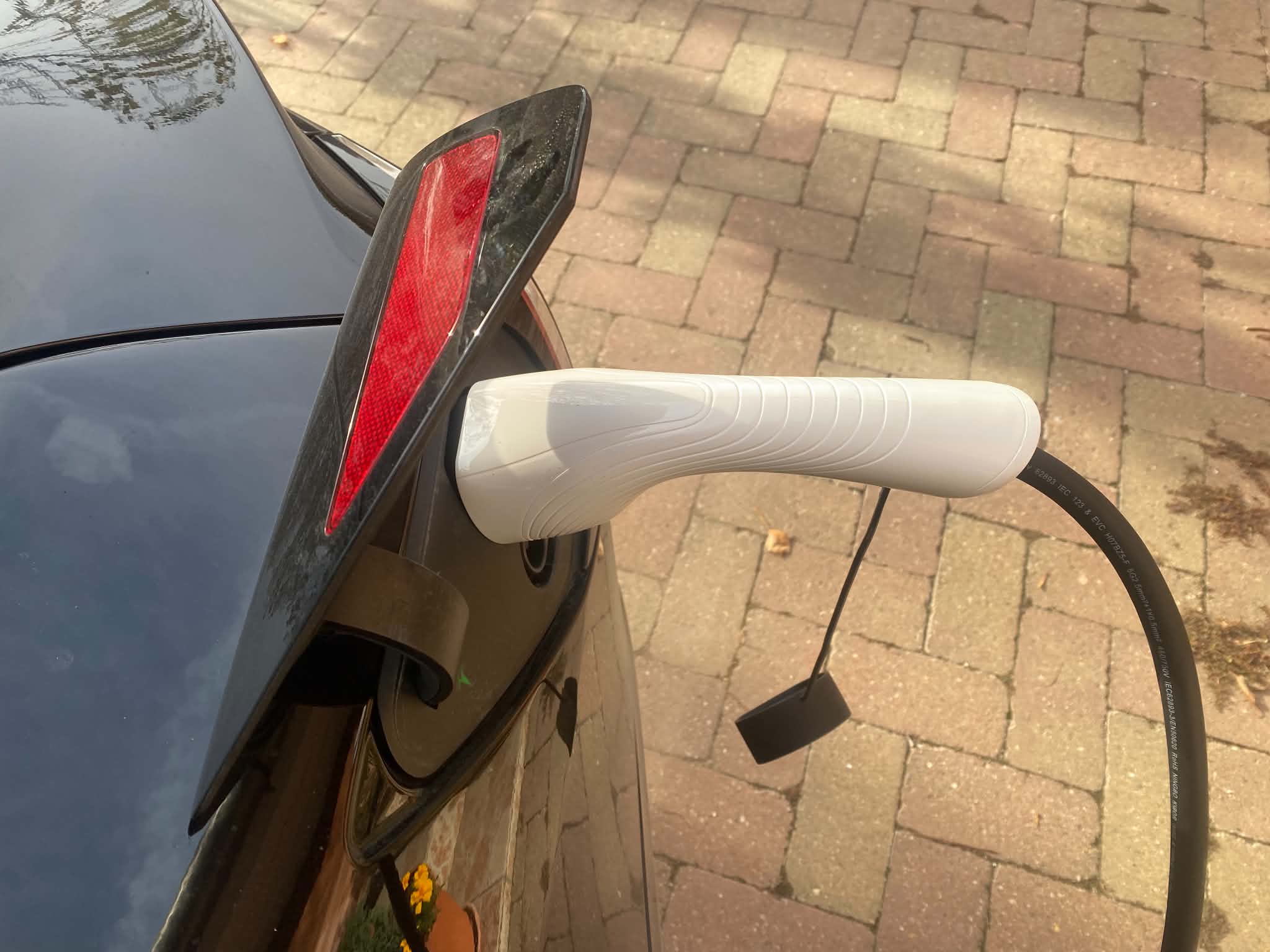 Fehér elektromosautó-töltő csatlakozója egy fekete Tesla töltőnyílásába dugva, otthoni töltés közben.