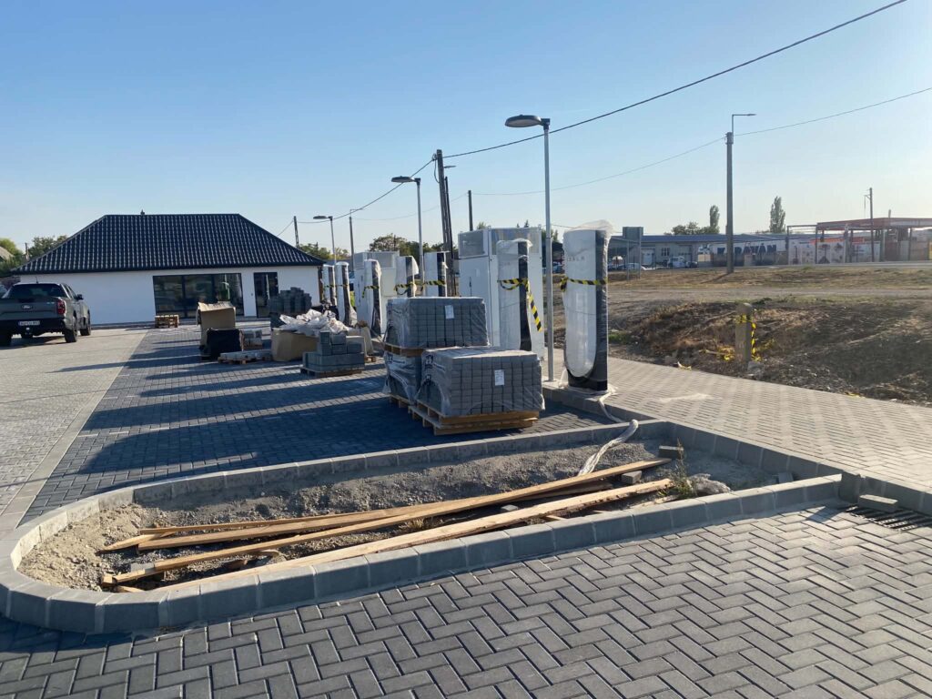 Épülő Tesla Supercharger Füzesabonyban, több becsomagolt töltőoszloppal és kiszolgálóépülettel.
